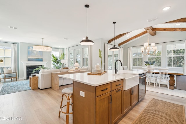 kitchen with sink, hanging light fixtures, light hardwood / wood-style flooring, an island with sink, and a high end fireplace