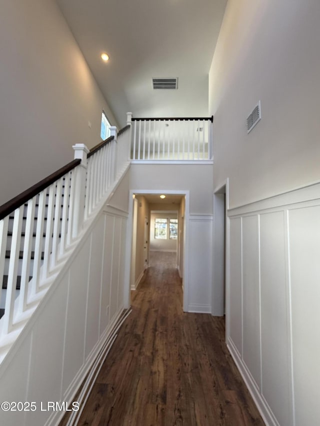 corridor with dark wood-type flooring and a towering ceiling