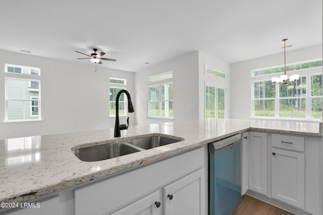 kitchen featuring pendant lighting, dishwasher, sink, white cabinets, and light stone counters