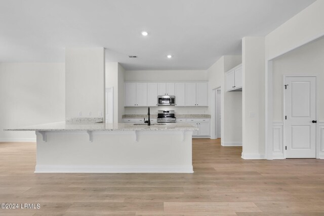 kitchen with light stone counters, a kitchen breakfast bar, white cabinets, and appliances with stainless steel finishes