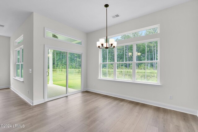 unfurnished dining area with plenty of natural light, a chandelier, and light wood-type flooring