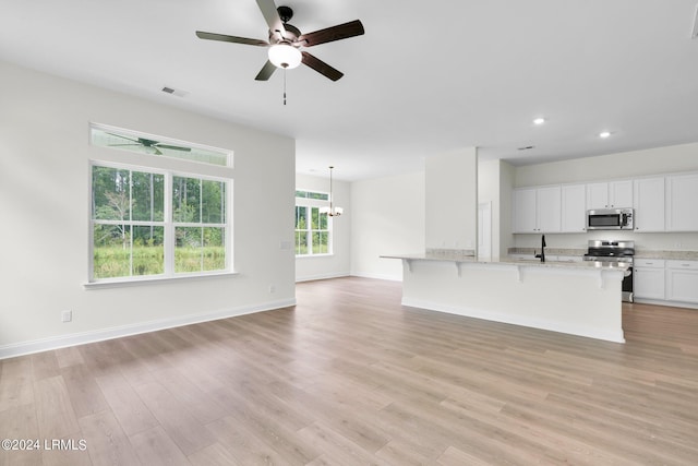 unfurnished living room with sink, ceiling fan with notable chandelier, and light wood-type flooring