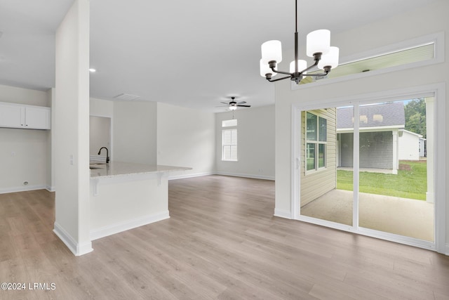 kitchen featuring sink, light stone countertops, white cabinets, decorative light fixtures, and light wood-type flooring