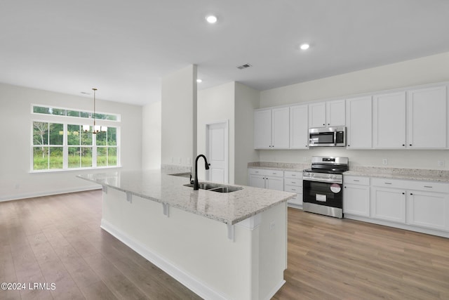 kitchen with white cabinetry, appliances with stainless steel finishes, light stone counters, and decorative light fixtures