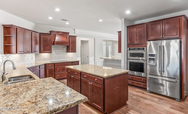 kitchen with stainless steel appliances, premium range hood, light stone countertops, and sink