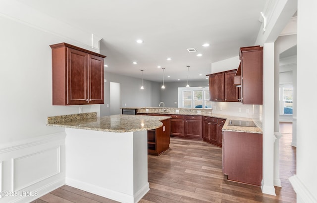 kitchen featuring decorative light fixtures, a kitchen breakfast bar, kitchen peninsula, light stone countertops, and light wood-type flooring