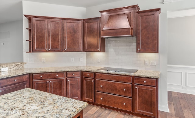 kitchen with black electric stovetop, custom exhaust hood, light stone countertops, and light wood-type flooring