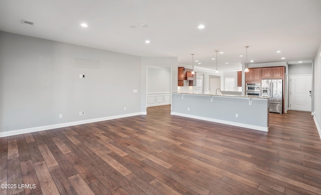 kitchen with dark hardwood / wood-style flooring, appliances with stainless steel finishes, a kitchen bar, and decorative light fixtures