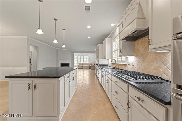 kitchen featuring premium range hood, stainless steel gas cooktop, hanging light fixtures, ornamental molding, and a kitchen island