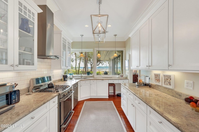 kitchen featuring a sink, appliances with stainless steel finishes, wall chimney exhaust hood, glass insert cabinets, and pendant lighting