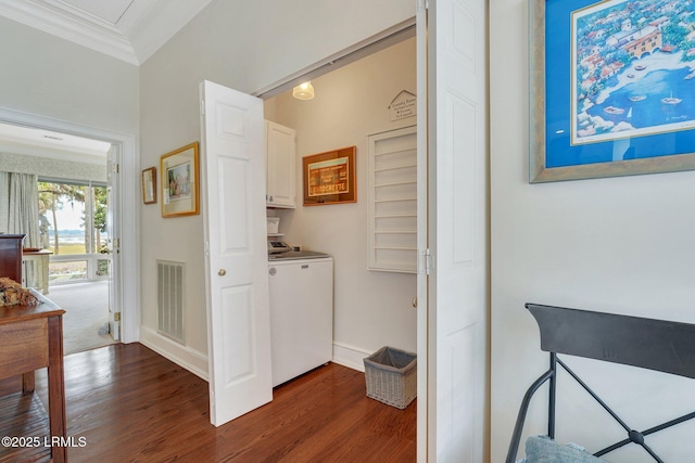 hall featuring dark wood-type flooring, visible vents, baseboards, washer / dryer, and crown molding