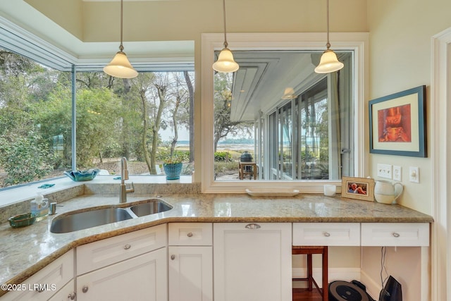 kitchen with decorative light fixtures, a sink, white cabinetry, and light stone countertops