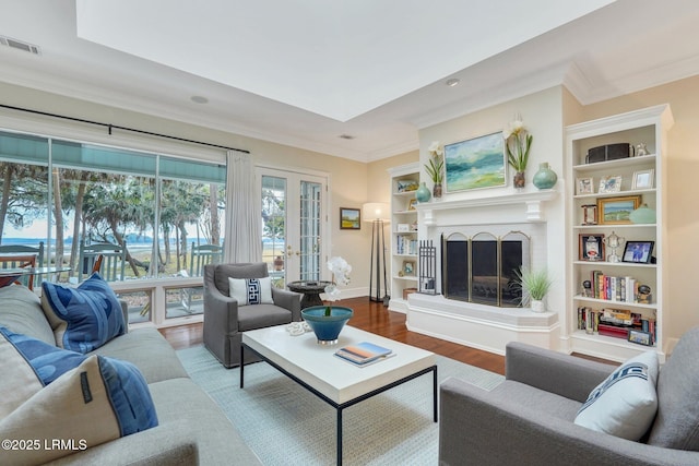 living room featuring french doors, crown molding, visible vents, a fireplace with raised hearth, and wood finished floors