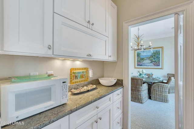 kitchen with dark stone counters, white cabinetry, a notable chandelier, and white microwave