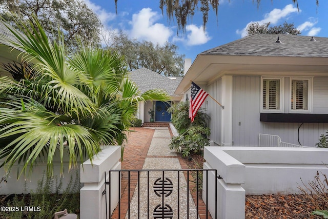 exterior space with roof with shingles, a fenced front yard, and a gate