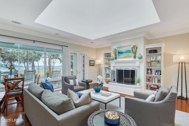 living area featuring a fireplace with raised hearth, visible vents, french doors, dark wood finished floors, and crown molding