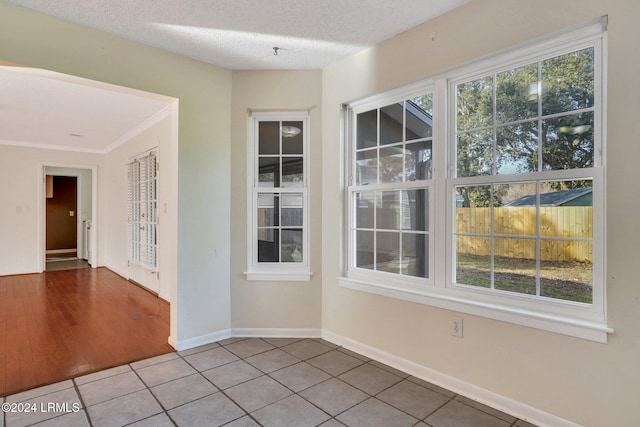 spare room with light tile patterned flooring, ornamental molding, and a textured ceiling