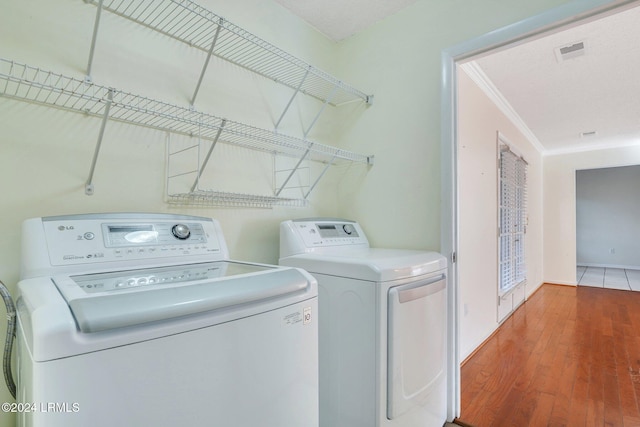 clothes washing area featuring hardwood / wood-style floors, ornamental molding, and washer and dryer