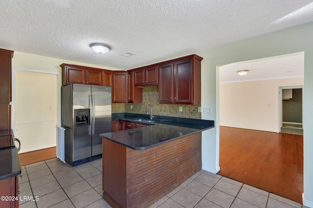 kitchen featuring sink, backsplash, stainless steel refrigerator with ice dispenser, light tile patterned flooring, and kitchen peninsula