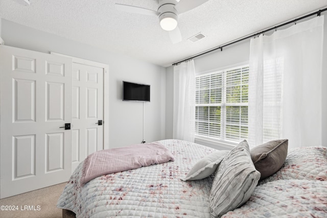 bedroom with ceiling fan, light colored carpet, and a textured ceiling