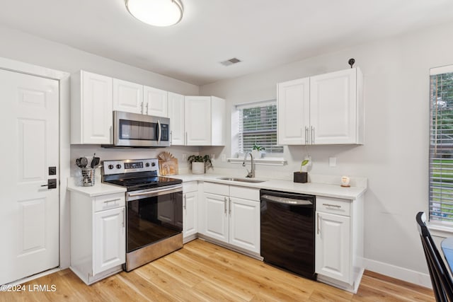 kitchen with light wood-type flooring, appliances with stainless steel finishes, sink, and white cabinets