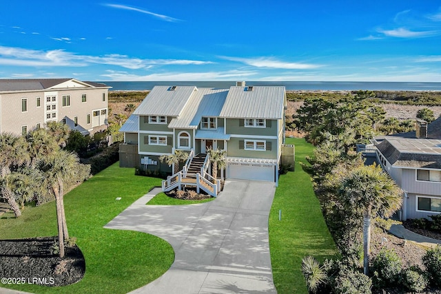 coastal home with metal roof, an attached garage, stairs, concrete driveway, and a front lawn