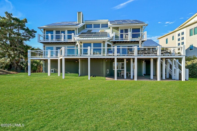 rear view of house with a deck, a yard, stairs, and roof mounted solar panels