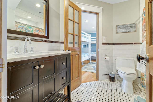 full bathroom featuring toilet, vanity, tile walls, wainscoting, and ensuite bath