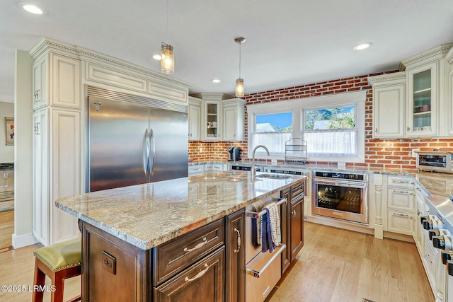 kitchen featuring light stone counters, cream cabinetry, light wood finished floors, stainless steel appliances, and a sink