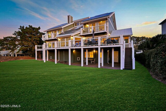 back of house at dusk with a patio area, a deck, solar panels, and a yard