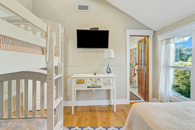 bedroom featuring lofted ceiling, wainscoting, wood finished floors, and visible vents