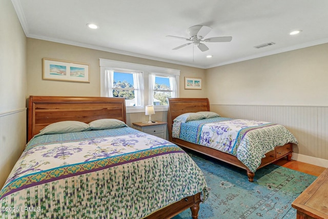 bedroom featuring visible vents, a ceiling fan, wainscoting, ornamental molding, and wood finished floors