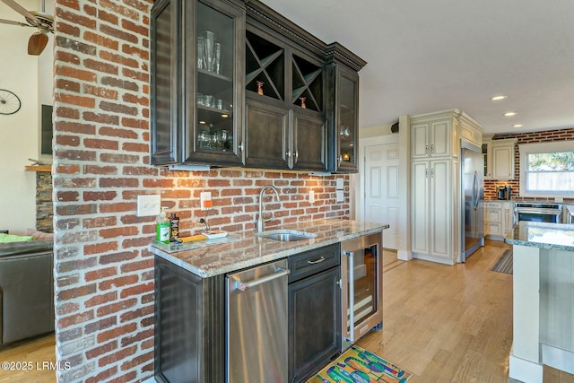 kitchen featuring beverage cooler, light wood-style flooring, light stone countertops, stainless steel built in refrigerator, and a sink