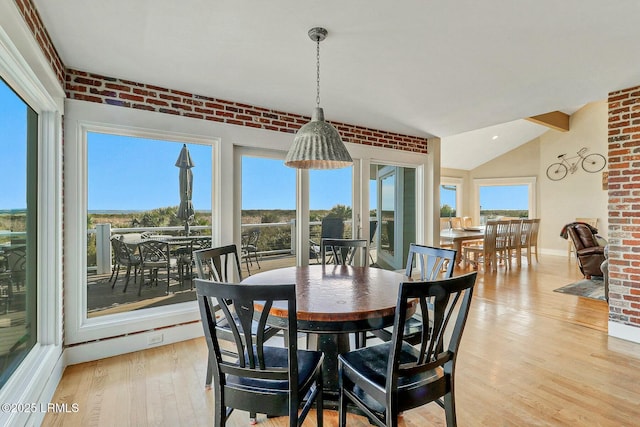 dining space with light wood finished floors, brick wall, baseboards, and vaulted ceiling