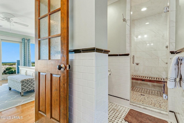 bathroom with a ceiling fan, ensuite bath, wood finished floors, a shower stall, and tile walls