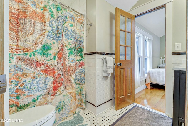 full bath with toilet, a wainscoted wall, tile walls, vaulted ceiling, and a shower with curtain