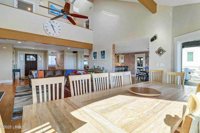 dining room featuring a high ceiling, ceiling fan, beamed ceiling, and wood finished floors