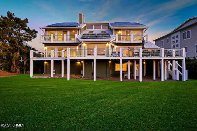 rear view of property with a patio, a chimney, solar panels, a lawn, and a deck