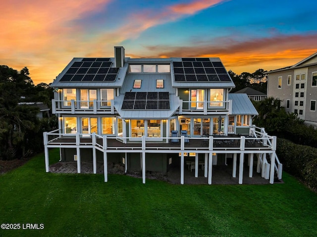 back of house at dusk with metal roof, a balcony, a lawn, roof mounted solar panels, and a standing seam roof