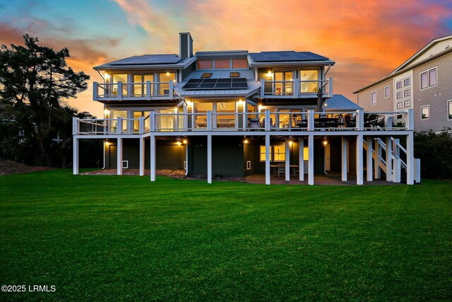 back of property with roof mounted solar panels, a deck, a lawn, and a patio