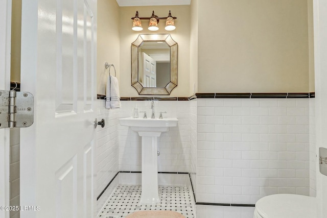 bathroom with toilet, a wainscoted wall, tile walls, and tile patterned floors