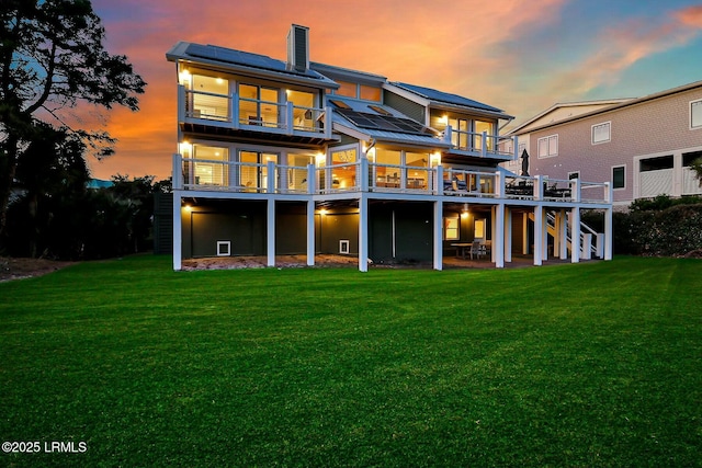 rear view of property with stairs, a yard, a wooden deck, roof mounted solar panels, and a chimney