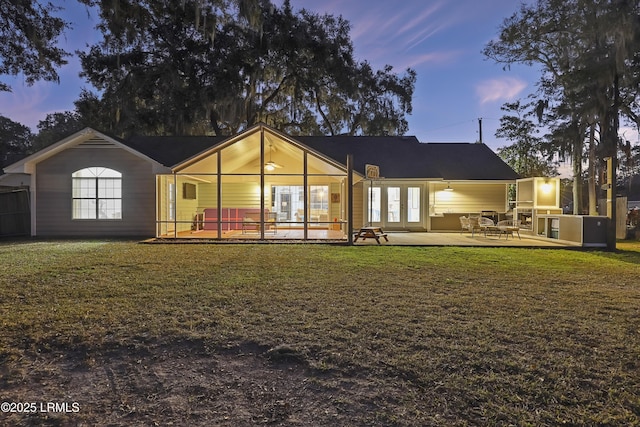 back house at dusk featuring a patio area and a lawn