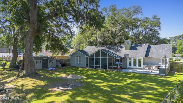 rear view of property with a shed, a patio area, a sunroom, and a lawn