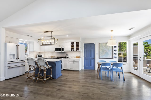 kitchen featuring white cabinetry, premium appliances, hanging light fixtures, a center island, and light stone counters