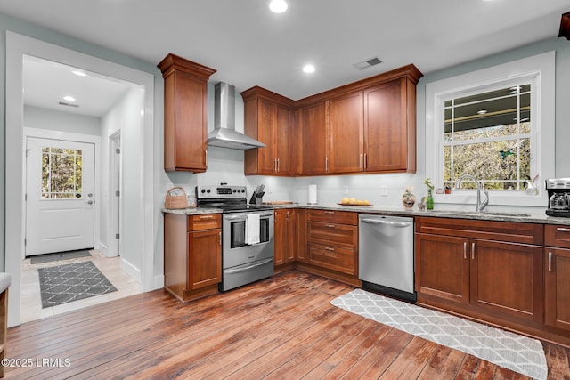 kitchen with appliances with stainless steel finishes, sink, light stone counters, and wall chimney exhaust hood