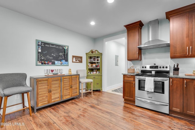 kitchen featuring electric stove, electric panel, light hardwood / wood-style floors, light stone countertops, and wall chimney exhaust hood