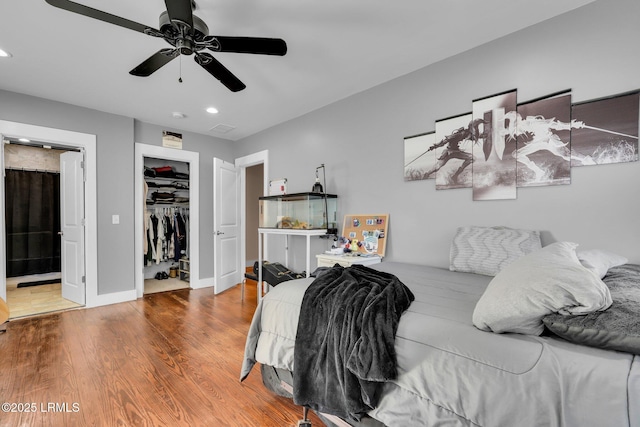 bedroom with ceiling fan, ensuite bathroom, wood-type flooring, a walk in closet, and a closet