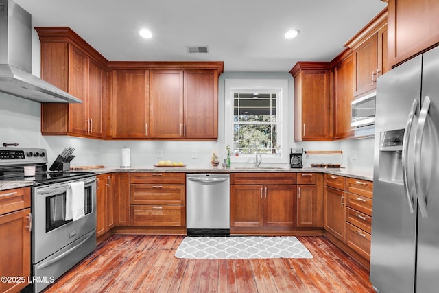 kitchen with light stone counters, wall chimney range hood, sink, and appliances with stainless steel finishes