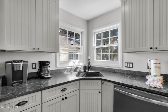 kitchen featuring stainless steel dishwasher, plenty of natural light, sink, and dark stone counters